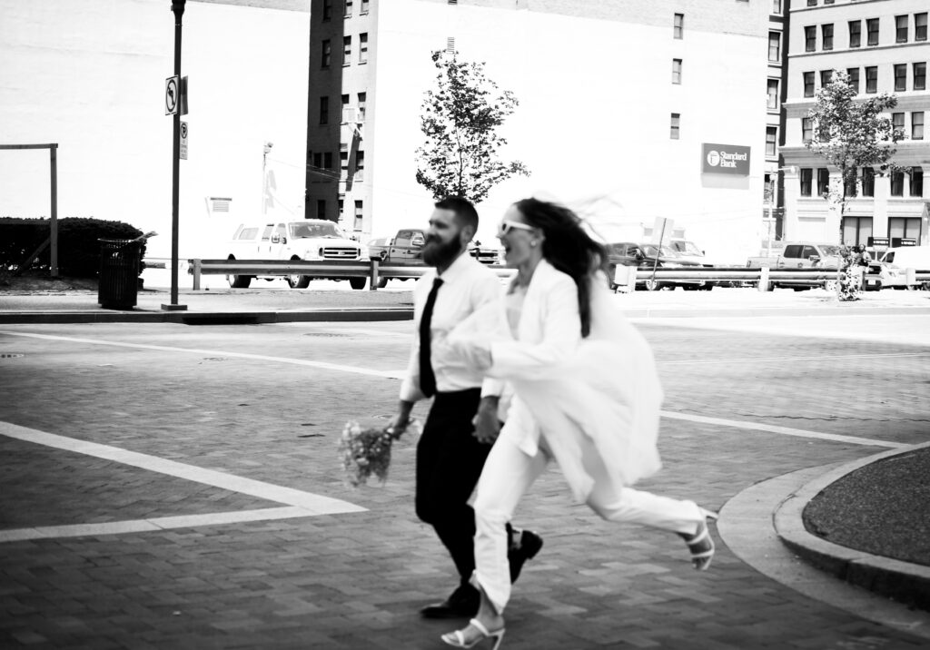 Couple skipping laughing in the streets of Downtown Pittsburgh after getting married at Allegheny Courthouse