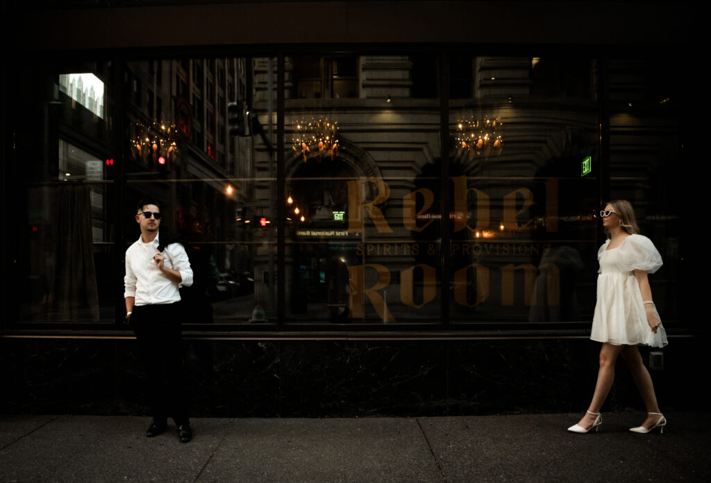 Bride walking towards standing groom wearing a chic white sort dress and white sunglasses in Downtown Pittsburgh
