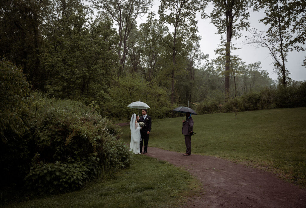 Bride and Groom standing with umbrellas and an officiant at Pittsburgh Botanic Garden