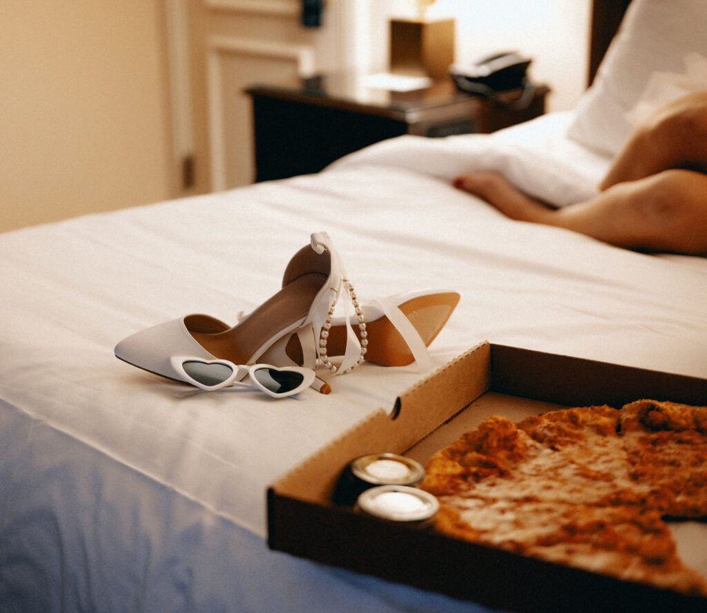 Wedding shoes with white glasses and pizza on a bed