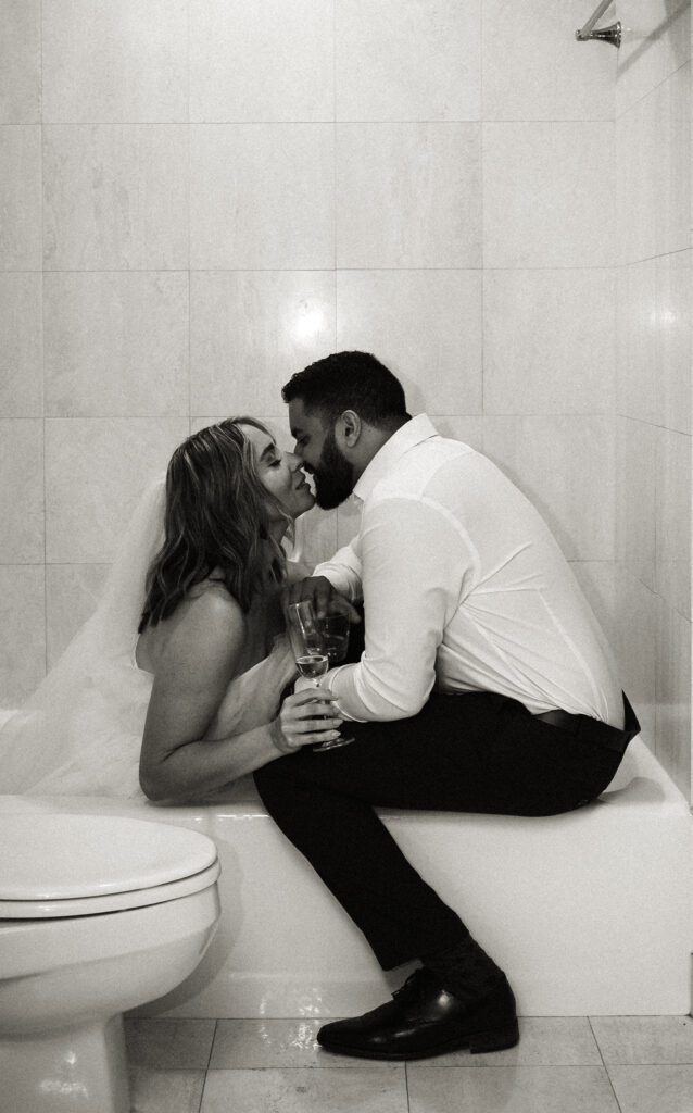 Bride and Groom about to kiss in a bathtub as they hold champagne glasses