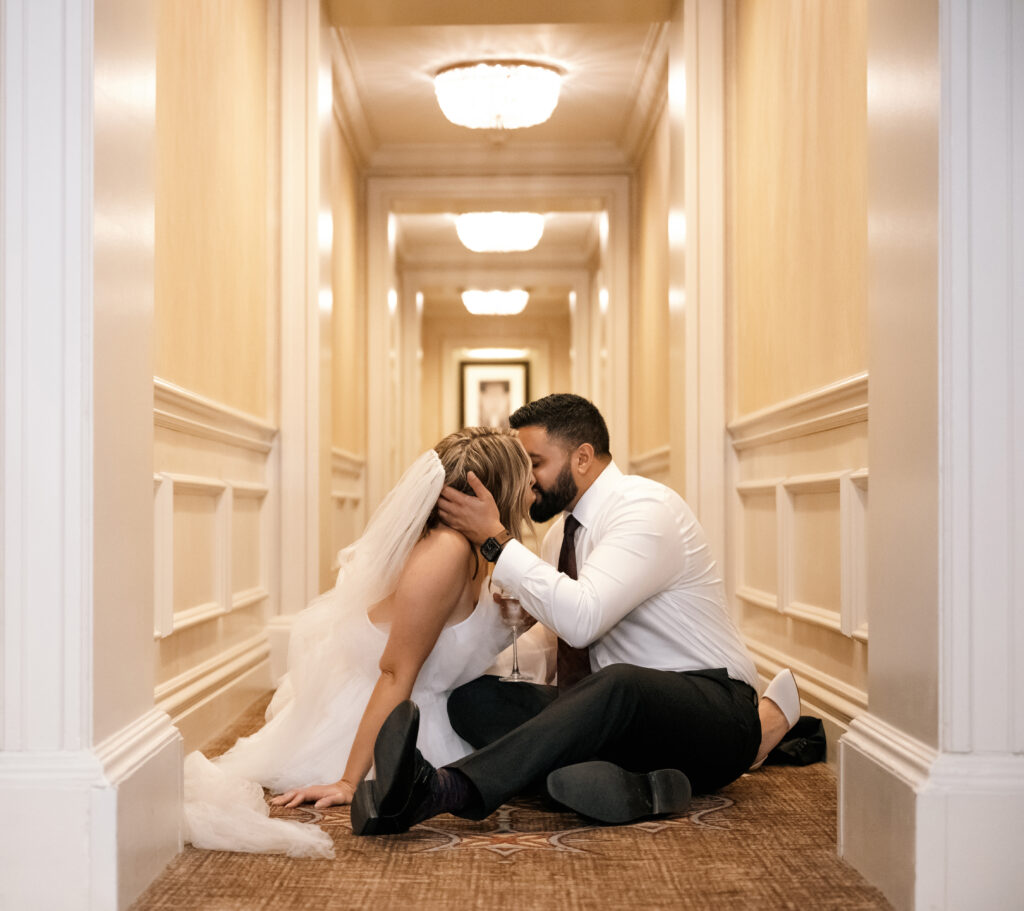 Bride and Groom kiss while sitting in the hallway of the Omni Penn Hotel