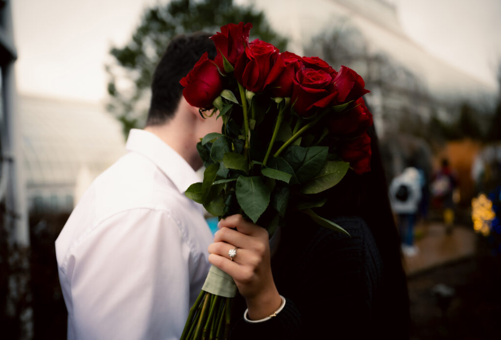 Red Roses in front of couple with engagement ring