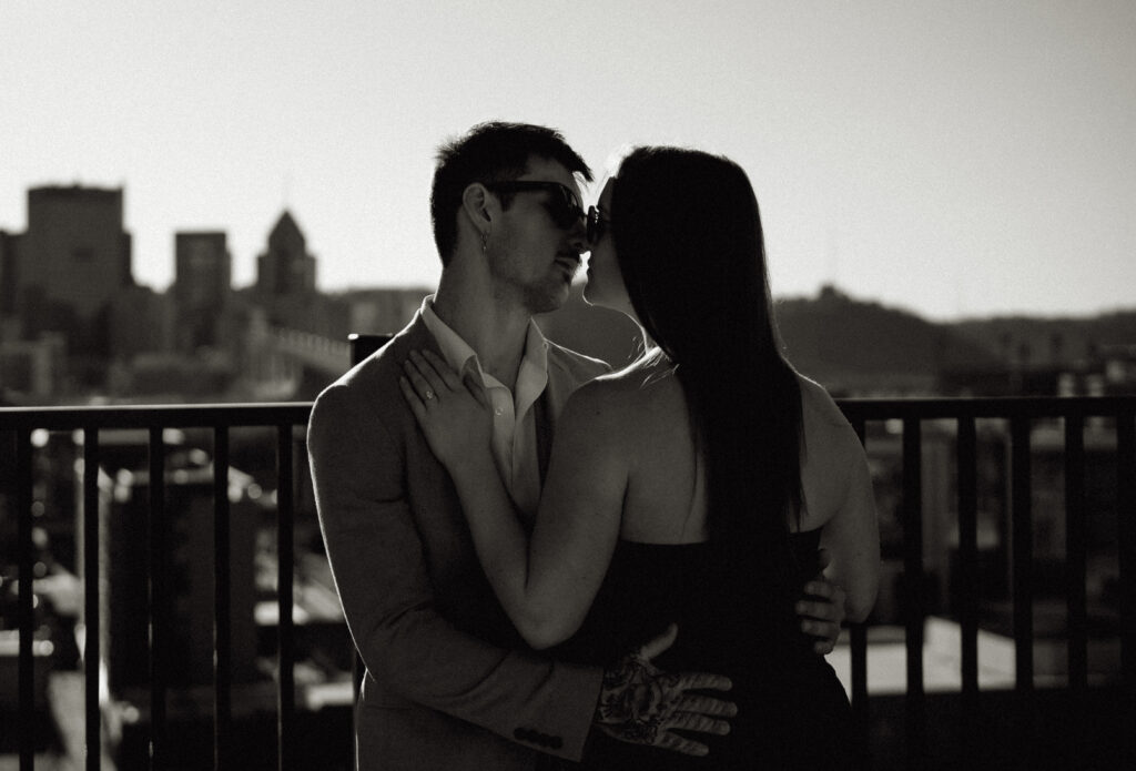 Couple kissing at Pittsburgh Rooftop with Downtown in the background.