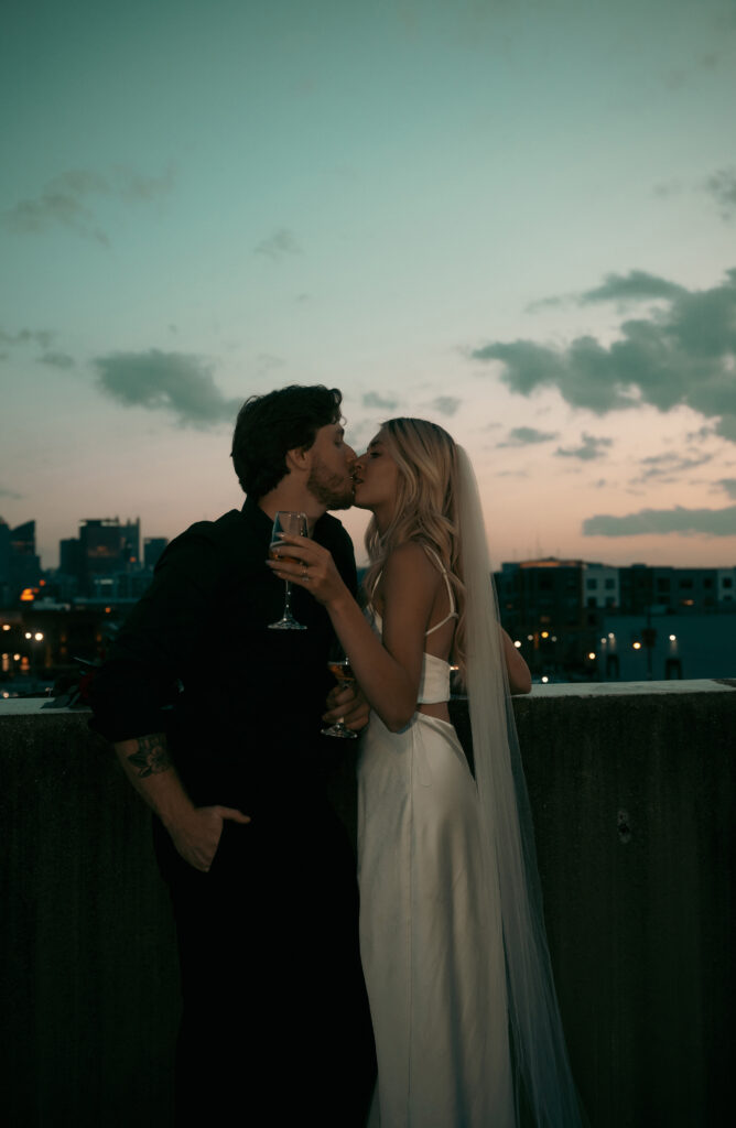 Couple kiss in front of Pittsburgh skyline with champagne and roses.