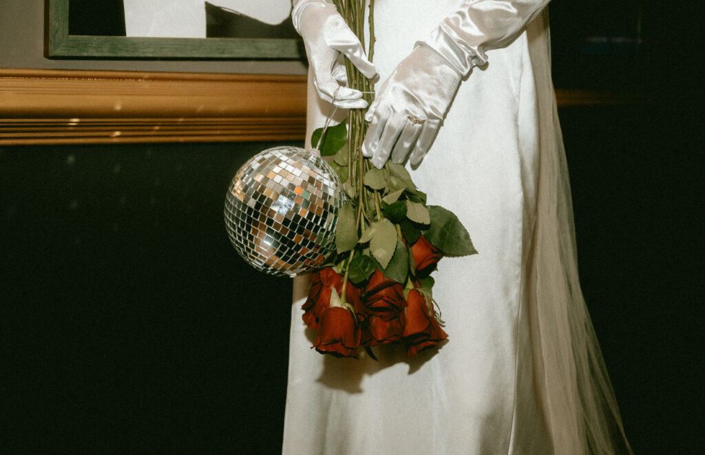 Bride holding a disco ball and red roses with white gloves at Row House Cinema