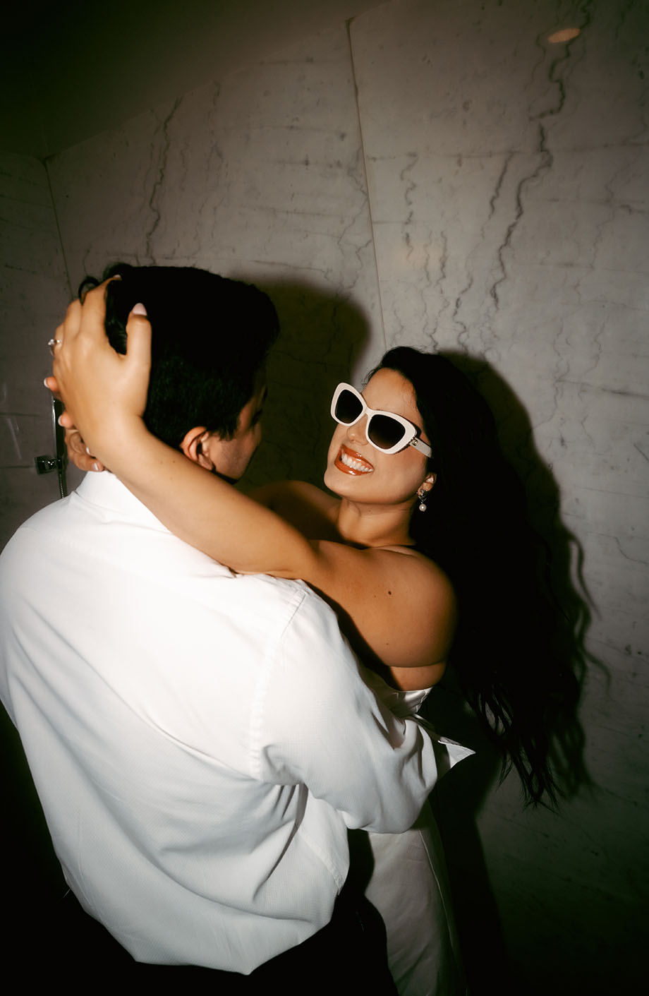 Bride wearing sunglasses looks at groom in hotel after engagement