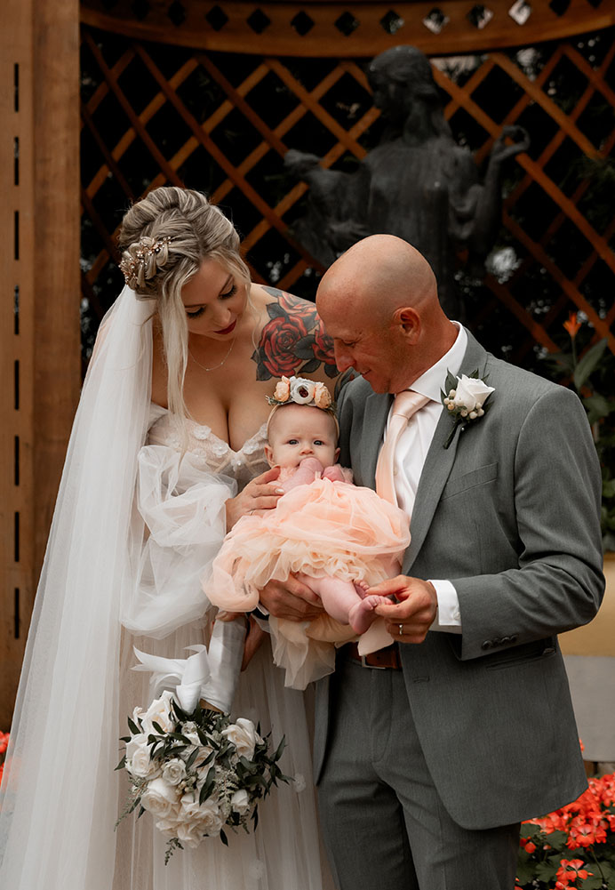 Bride and Groom hold their baby at their wedding in Phipps Conservatory and Botanical Garden