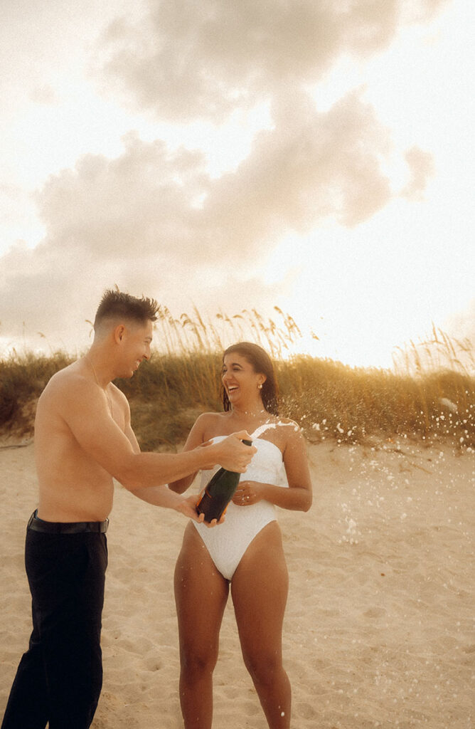 Engaged couple pop champagne at Beach Engagement