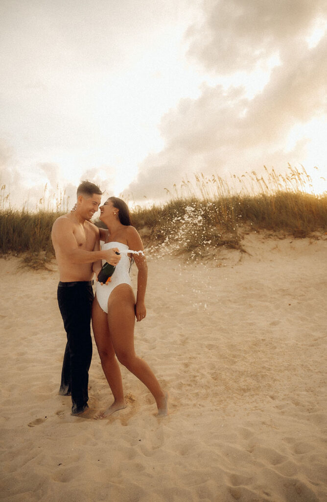 Engaged couple pop champagne at Beach Engagement