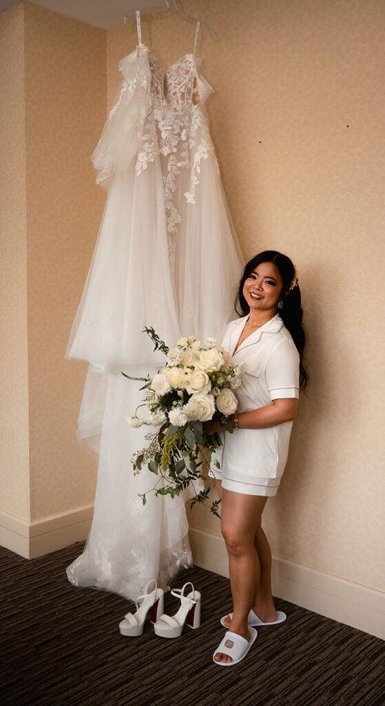 Bride standing next to her wedding gown holding her bouquet