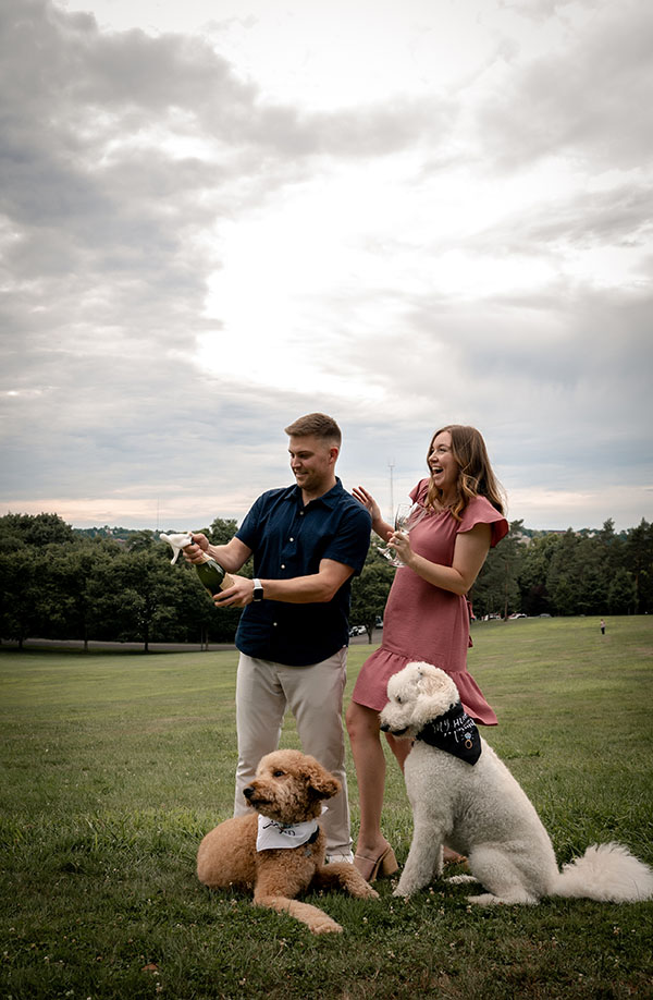 Couple popping a champagne bottle during engagement with their dogs