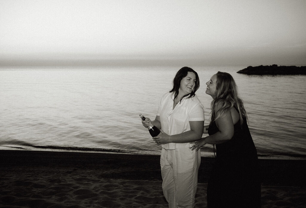 Couple popping champagne at Beach Engagement