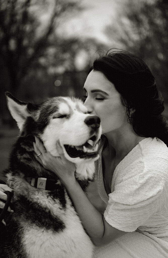 BW Warm documentary-style photo of couple kissing while holding their dogs’ leashes in an urban Pittsburgh setting.