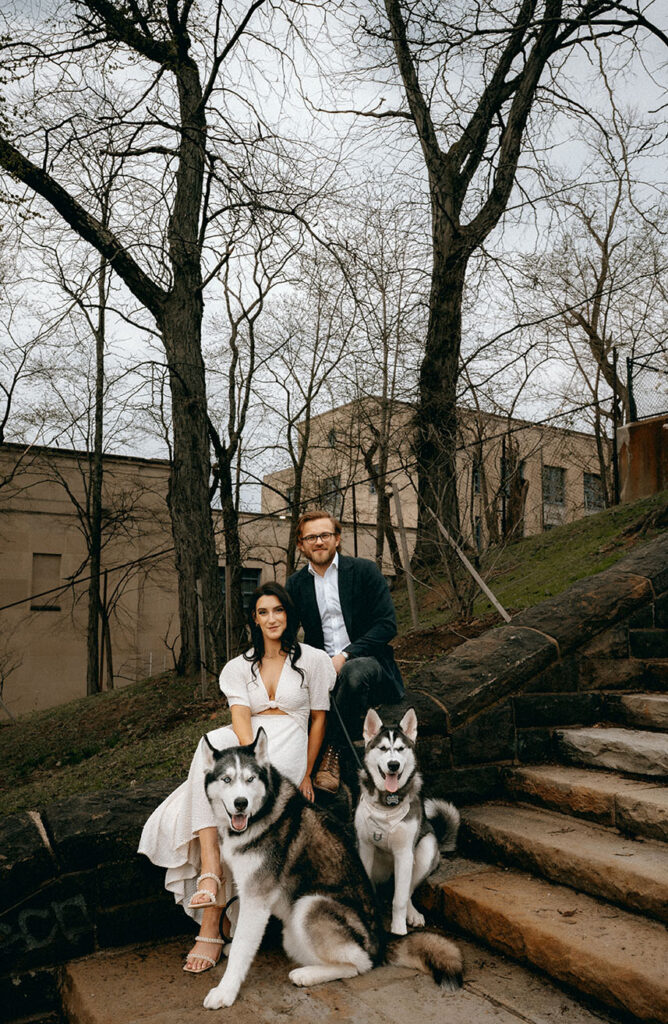 Family Photo of couple while their huskies sit on the sidewalk, capturing a personal moment.