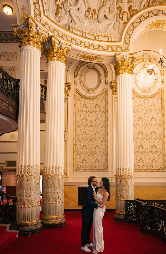 Couple standing on the grand staircase of Heinz Hall in formal attire during their engagement session in Pittsburgh.