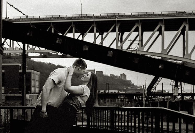 Artistic engagement photo of a couple in front of Pittsburgh’s downtown skyline from The Highline bridge platform.