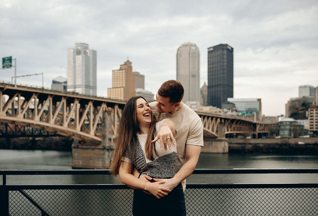 Playful documentary-style engagement photo at The Highline, showing Pittsburgh’s iconic bridges and skyline.