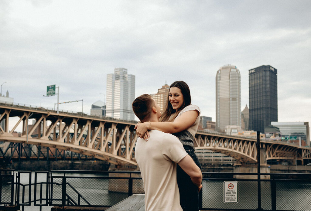 Stylish engagement pose at The Highline with Pittsburgh skyscrapers in the background and moody spring skies.