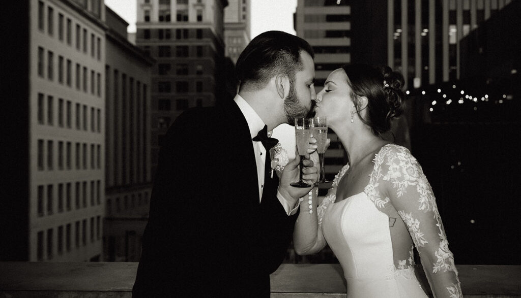 BW Bride and groom kissing with champagne glasses in front of them at the Cincinnati contemporary art museum