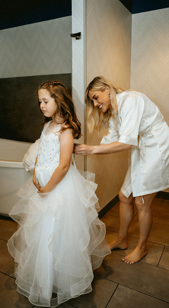 Bride helping daughter put on dress before getting married