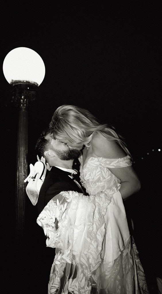 Bride and groom kiss at night while she holds on to her heels