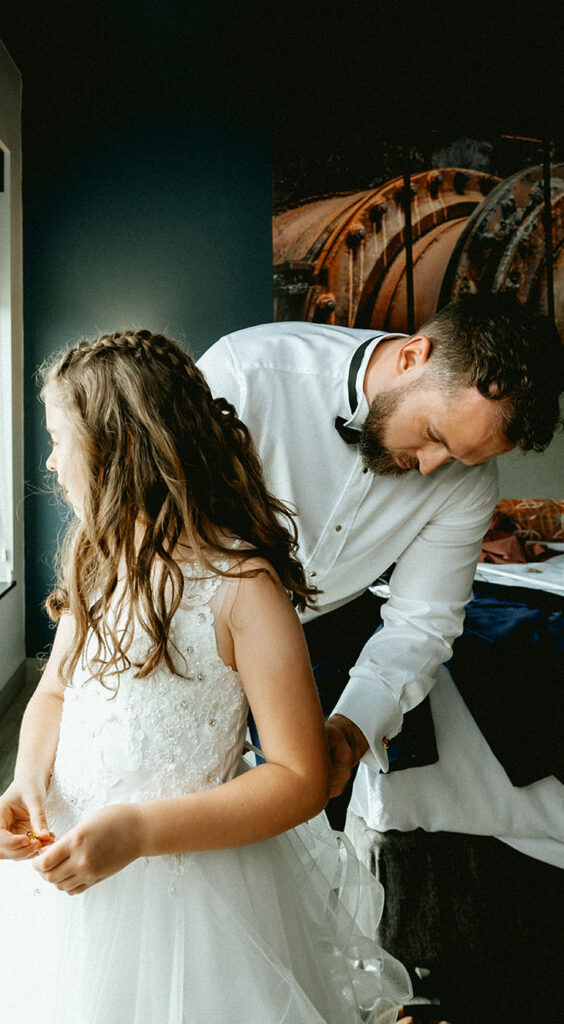 Groom helps daughter with her dress at Hotel Indigo before wedding