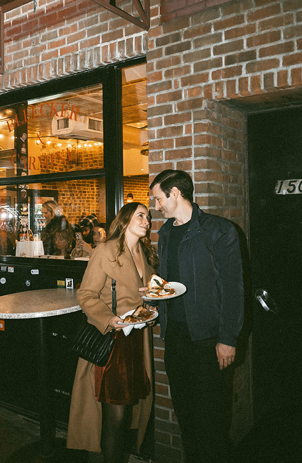 Couple grabbing pizza at Joe’s Pizza in New York City during a documentary engagement photo session.
