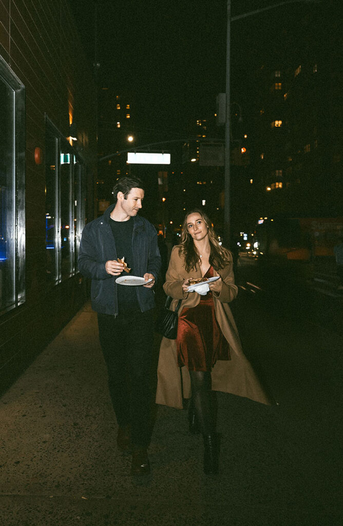 Cinematic engagement photos of a couple walking through New York City at night with neon lights and urban atmosphere.
