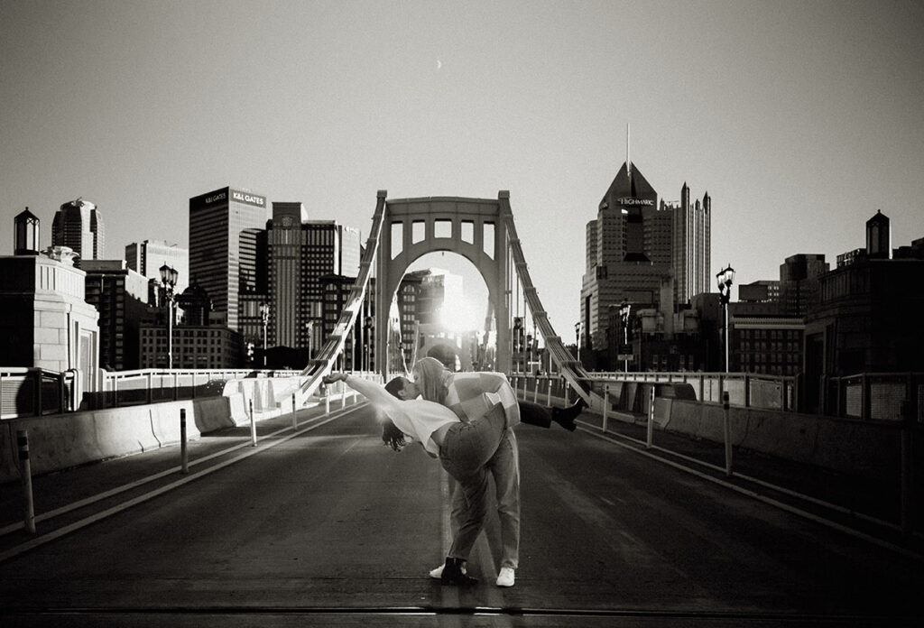 BW Cinematic couple photo on the Roberto Clemente Bridge with the Pittsburgh skyline at sunset.