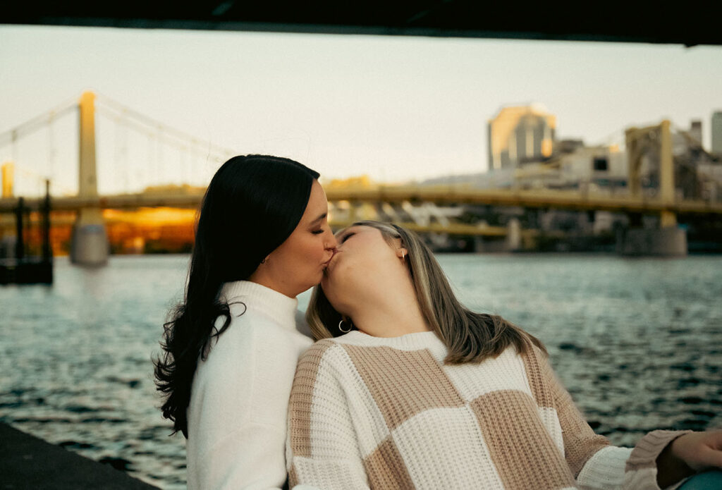 Romantic editorial photo of a couple kissing in front of the Pittsburgh skyline.