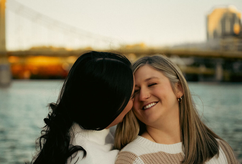 Romantic editorial photo of a couple kissing in front of the Pittsburgh skyline.