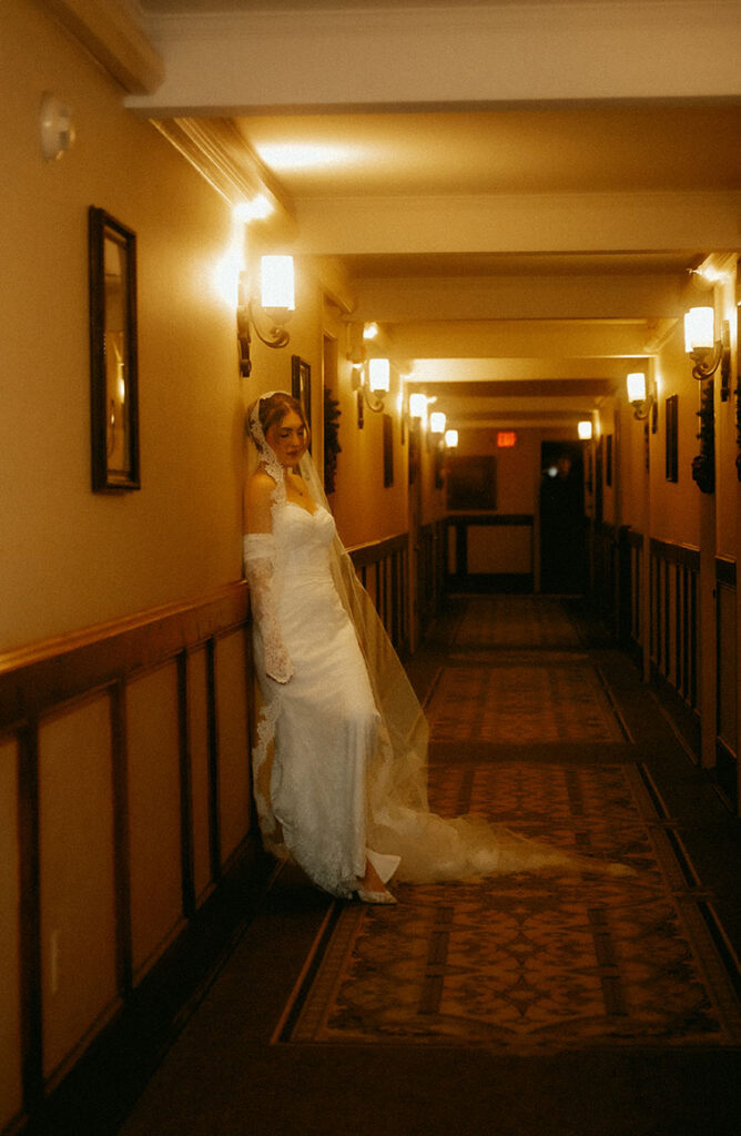 Bride in vintage wedding gown standing in the hallway with warm lighting at Skytop Lodge during winter wedding