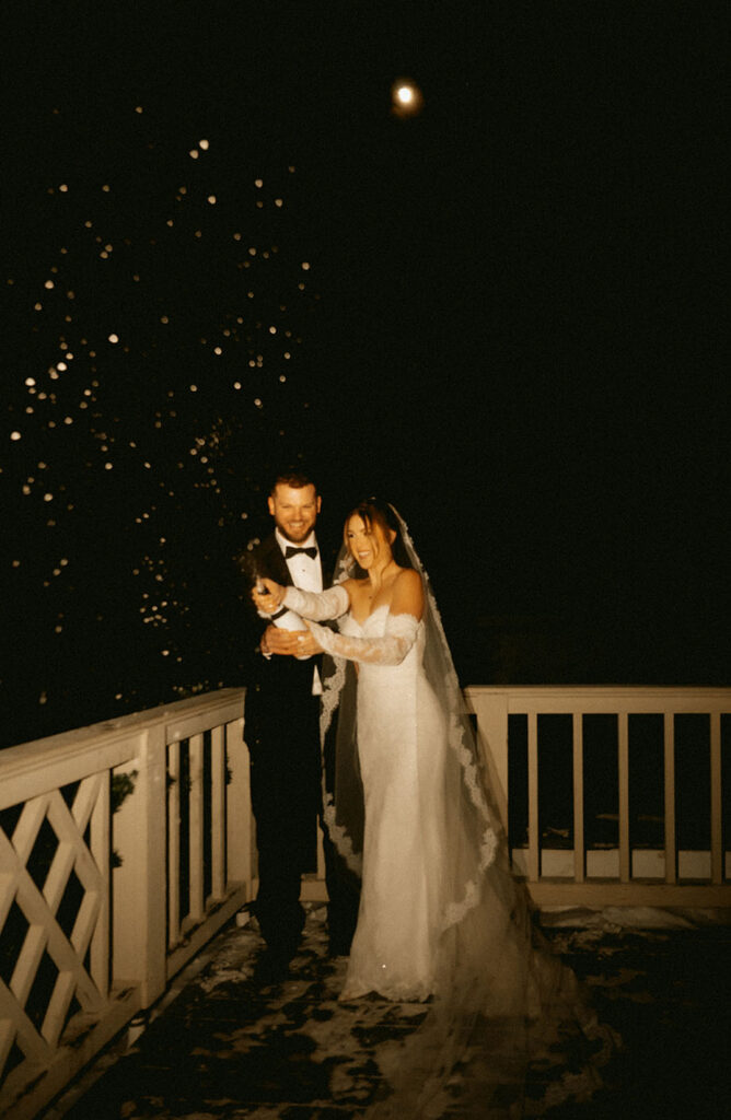 Bride and groom under the January Wolf Moon popping a champagne at Skytop Lodge winter wedding