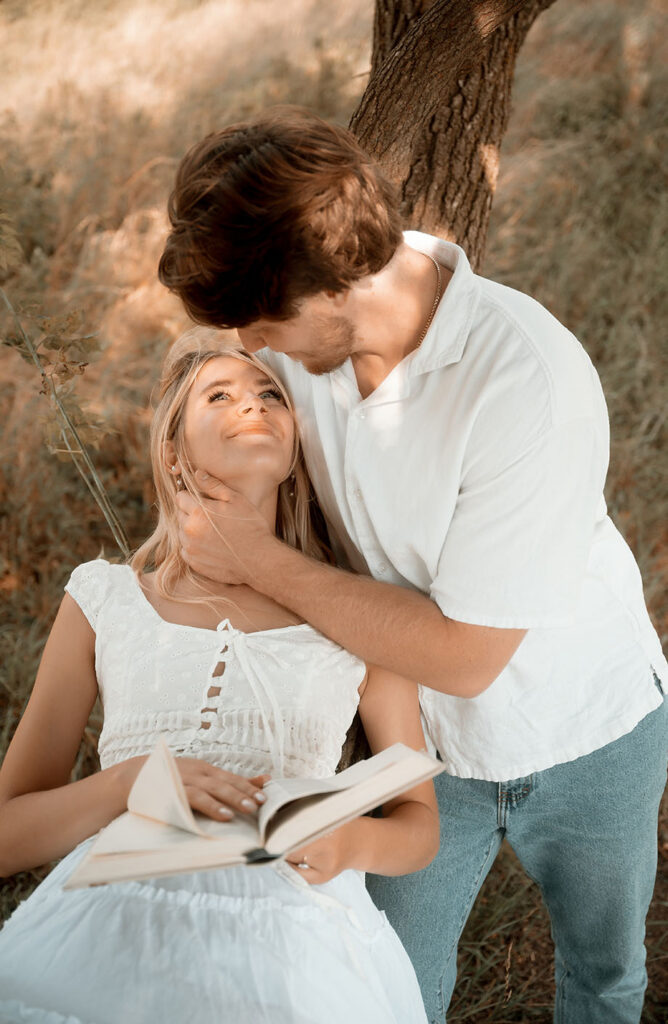 engagement session in Pittsburgh with couple reading together under tree in cinematic summer light