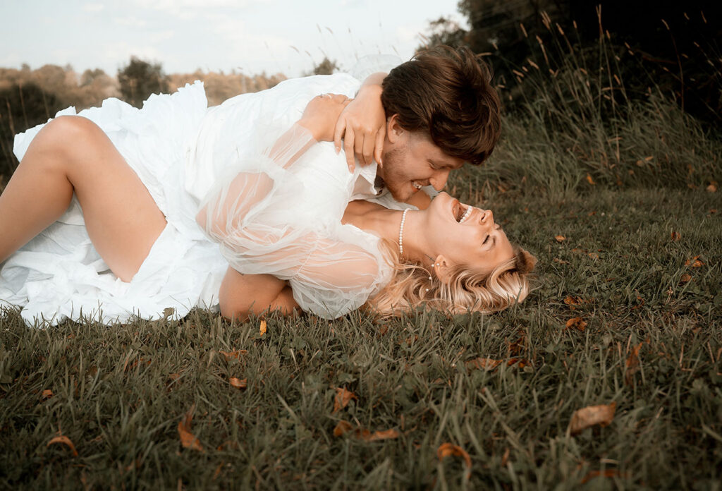 Couple laughing during summer engagement photo in Pittsburgh park rolling in the grass in cinematic documentary style