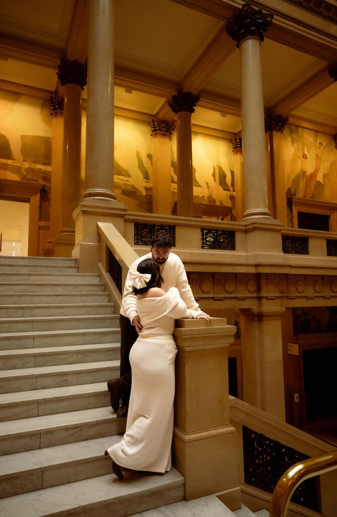 Cinematic engagement photo in Pittsburgh museum stairwell emphasizing scale, symmetry, and emotional connection