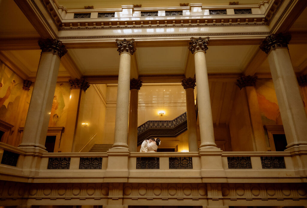 Romantic couple sitting on museum stairs in Pittsburgh creating cinematic engagement photos with architectural depth