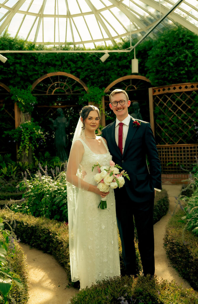Bride and groom embracing beneath her veil among lush tropical greenery at Phipps Conservatory.