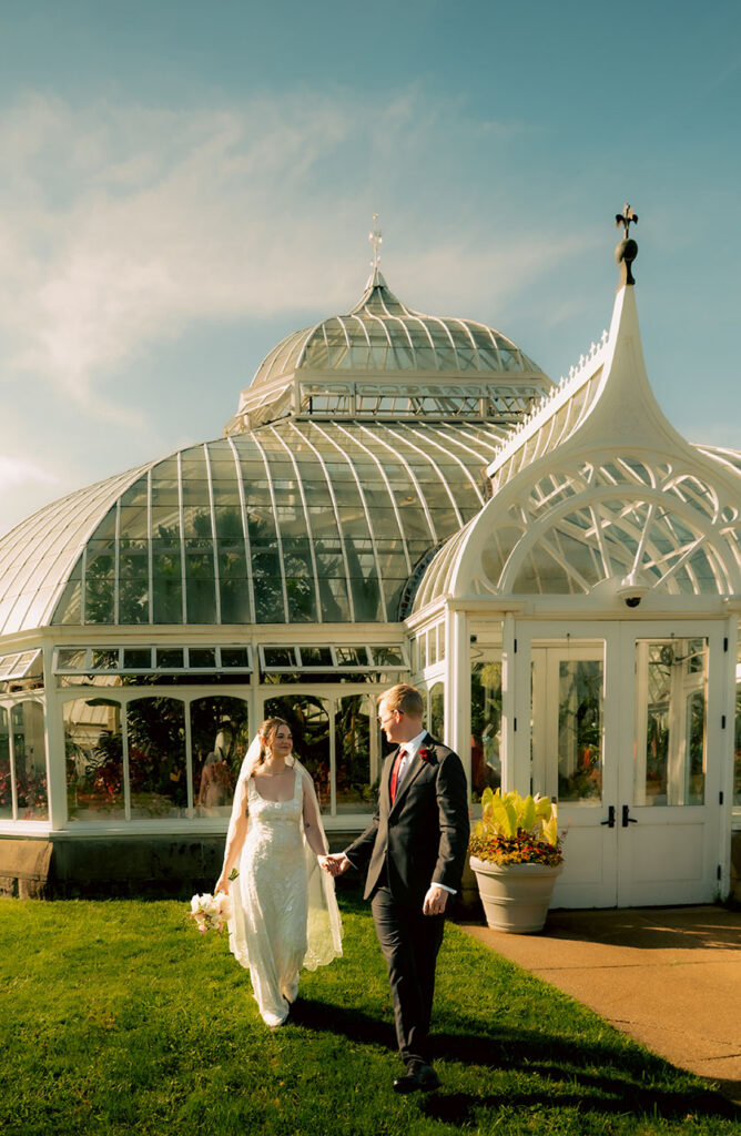 Bride and groom laughing together on a bench inside the sunlit Phipps Conservatory gardens.
