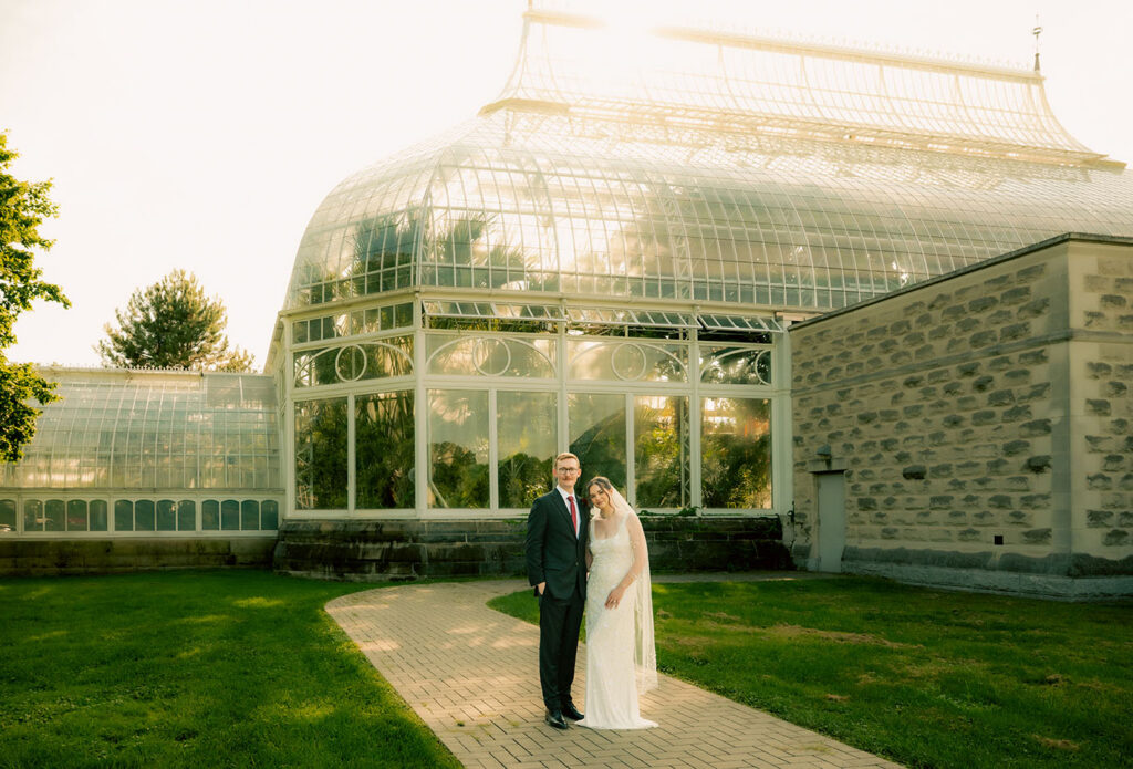 Newlyweds standing together among the formal gardens beneath the Phipps Conservatory glasshouse.