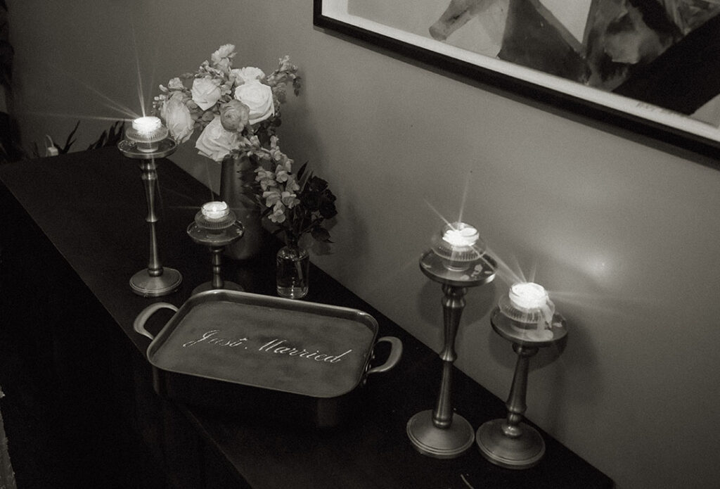 Black-and-white reception details with flowers, glowing candles, and a “Just Married” dessert at Balvanera.